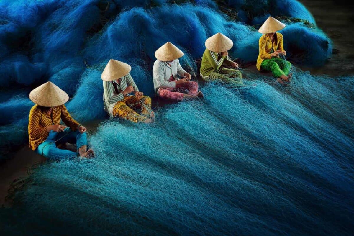 Vijf Vietnamese vrouwen zijn bezig met het repareren van visnetten