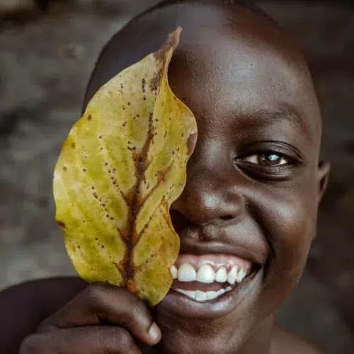 Ibrahim-Rashid-Otieno-A-simple-smile-500x500 Een lachend Afrikaans jongetje verschuilt zich achter een groot blad van een boom